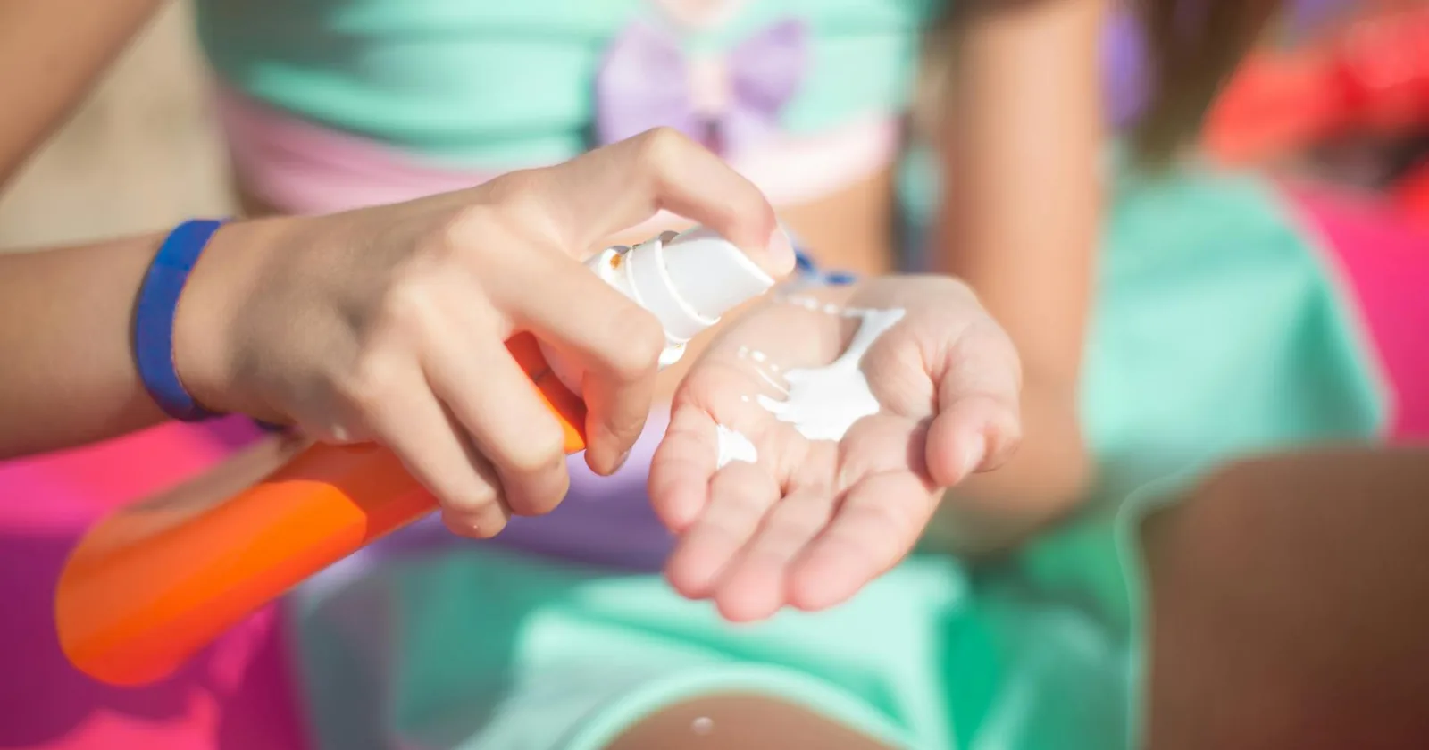 A person sprays sunscreen lotion onto their palm before applying it, the everyday ritual at the heart of the sunscreen and vitamin D debate.